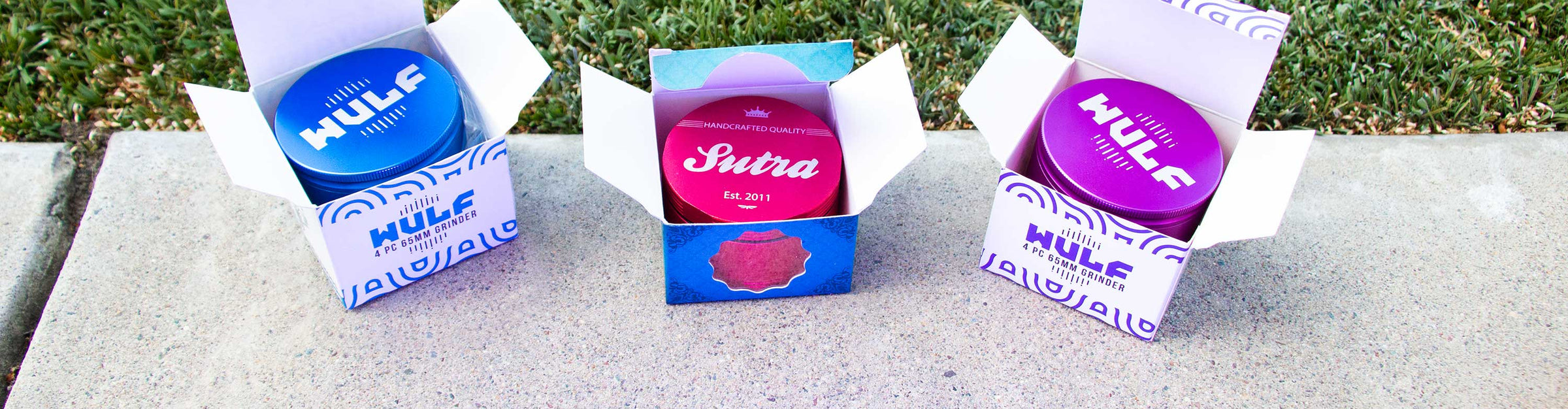 Sutra and Wulf Grinders standing inside boxes outside on cement walkway near grass by building