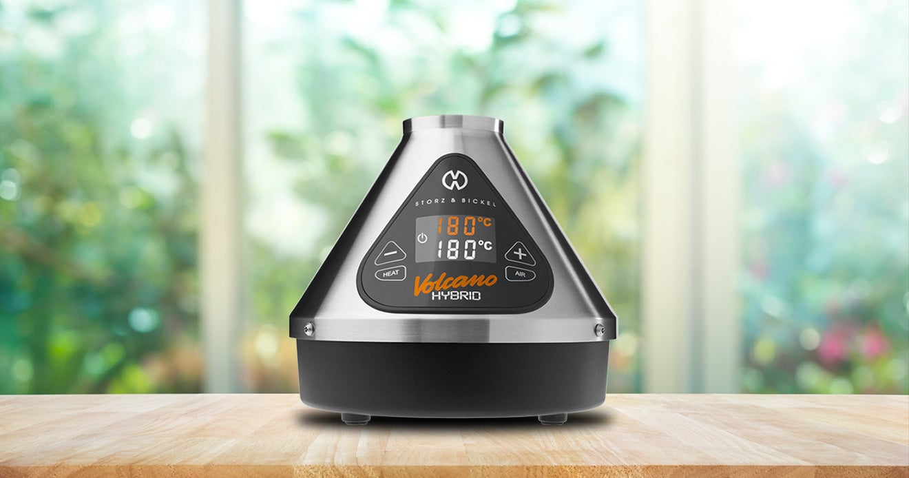 Storz and Bickel Volcano Hybrid standing on wooden table inside home with bushes in background.