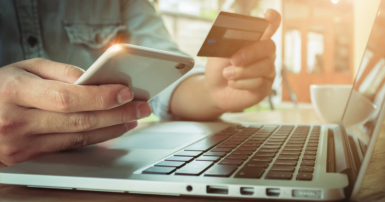Man shopping online with credit card and phone with sun going through window