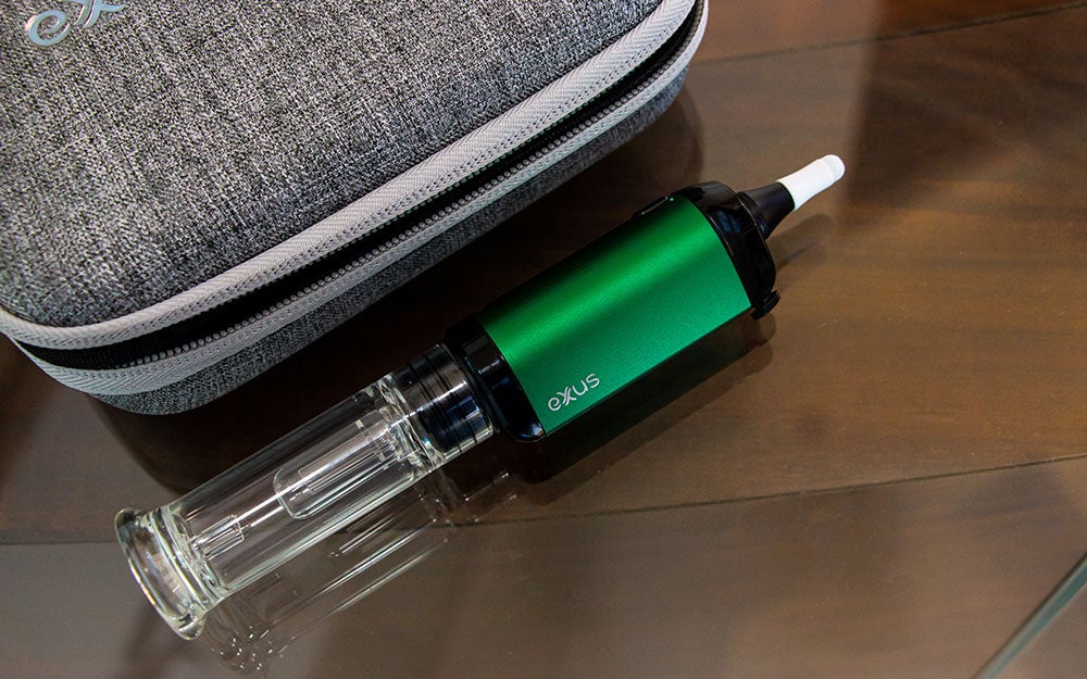 Exxus VRS Nectar Collector Mode standing on wooden table with glass top next to carrying case