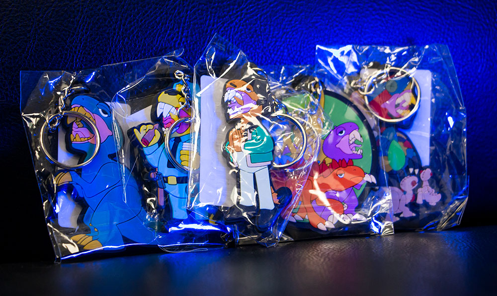 Elbo Glass Dancing Dinos keychains in a packet under coloured lighting