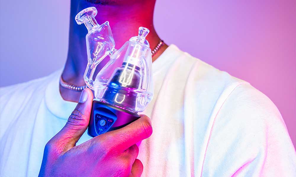 Person holding a Sutra DBR Pro electronic rig with its glass attachment under pink and purple lighting