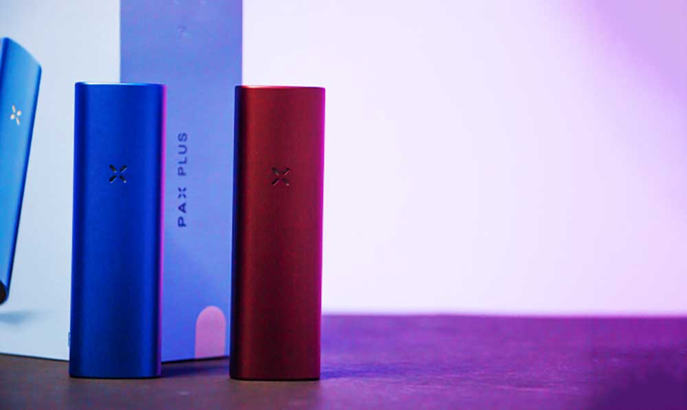 PAX Plus vaporizers standing beside their retail boxes against a pastel background