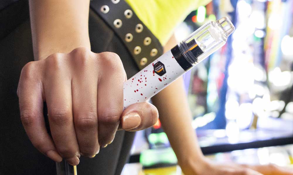 Hand holding a white WULF Orbit concentrate vaporizer above a dark workbench