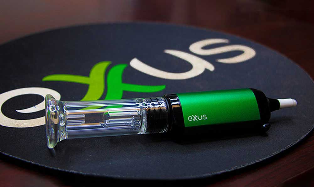 Green Exxus VRS concentrate vaporizer resting on a black Exxus branded mat