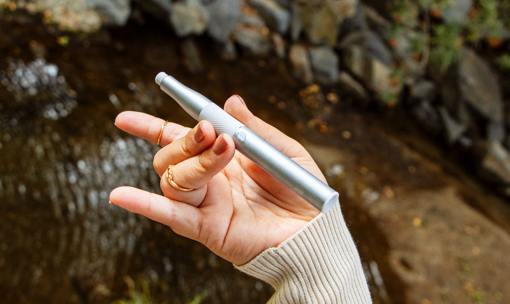 Woman holding Puffco New Plus by a creek under natural lighting