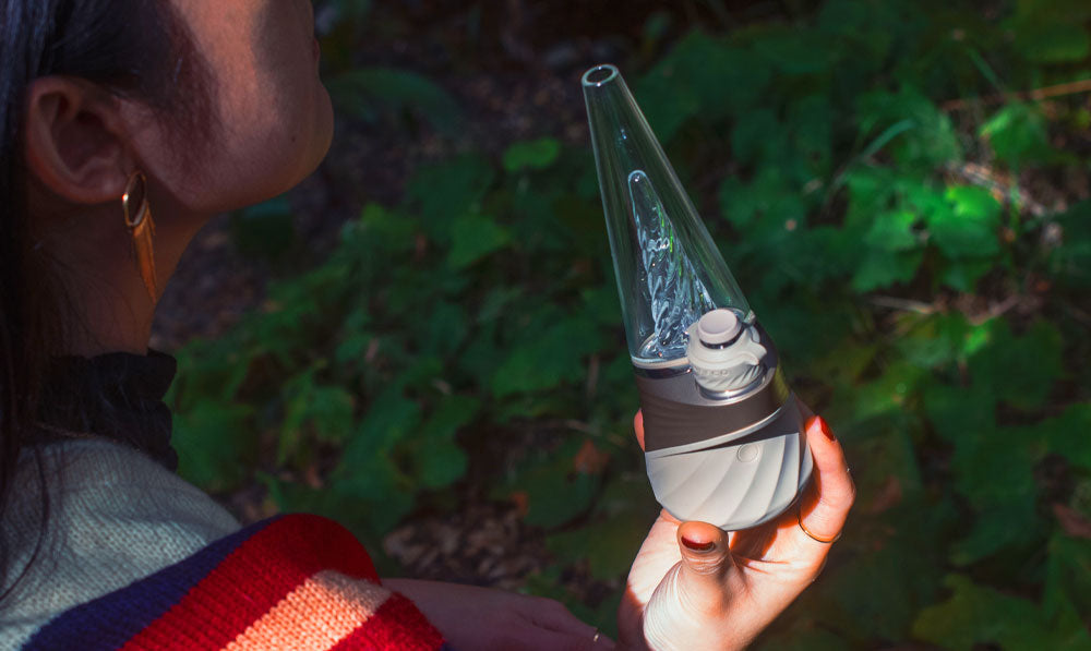 Woman holding Puffco New Peak Pro Desert by forest trail