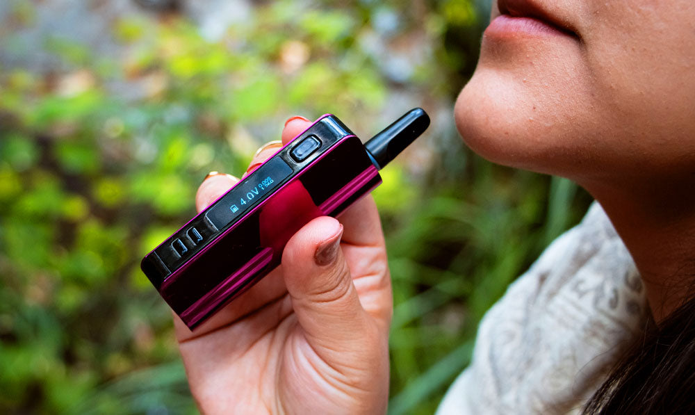 Woman holding Exxus Snap VV Pro near mouth in front of forest trail