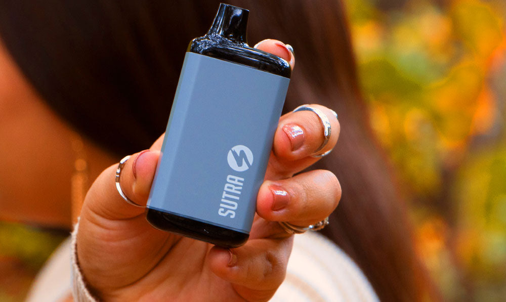 Woman holding Sutra SILO Pro in front of park trail with flowers nearby