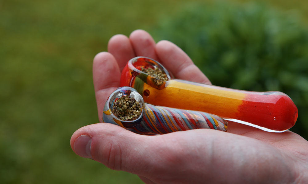 Man holding two glass pipes in palm over grass