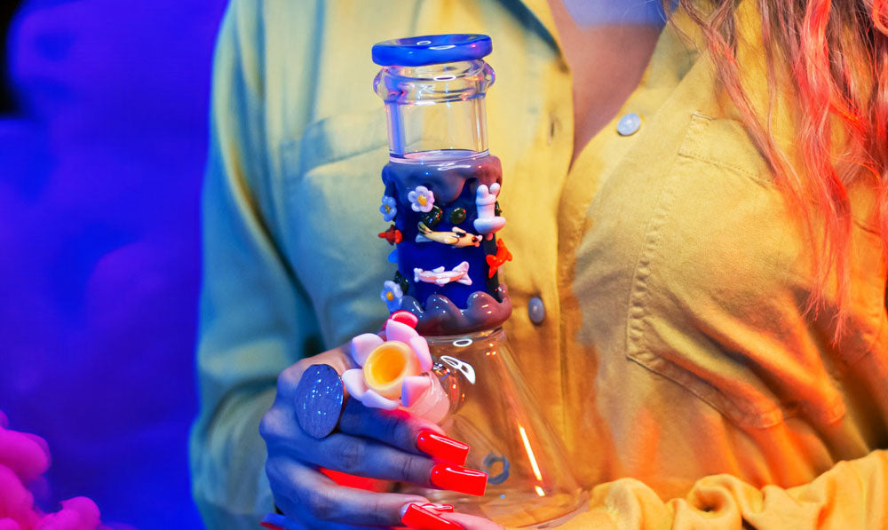 Woman holding Empire Glassworks Koi Pond Baby Beaker in front of blue studio background with smoke clouds nearby