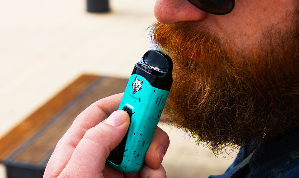 Bearded person holding a teal WULF Flex dual use vaporizer