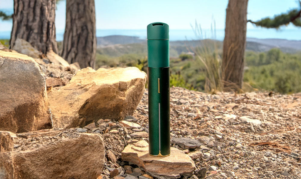 Puffco Limited Edition Pine on rocky terrain with pine trees in the background