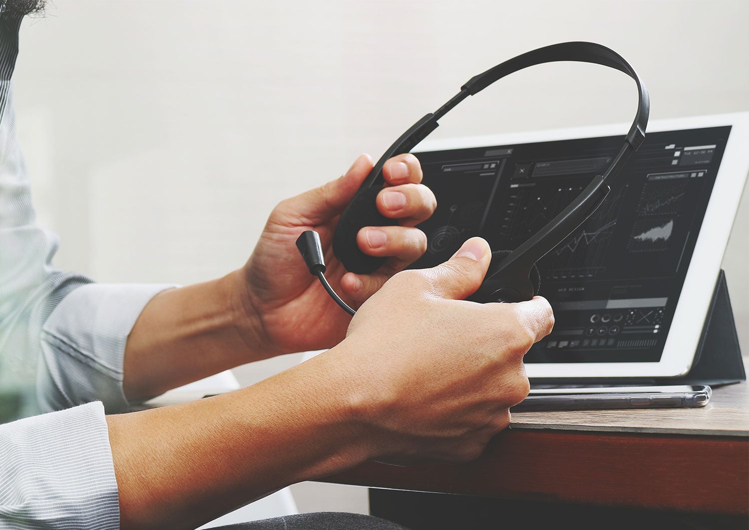 Person holding a headset at a desk in front of a tablet showing charts