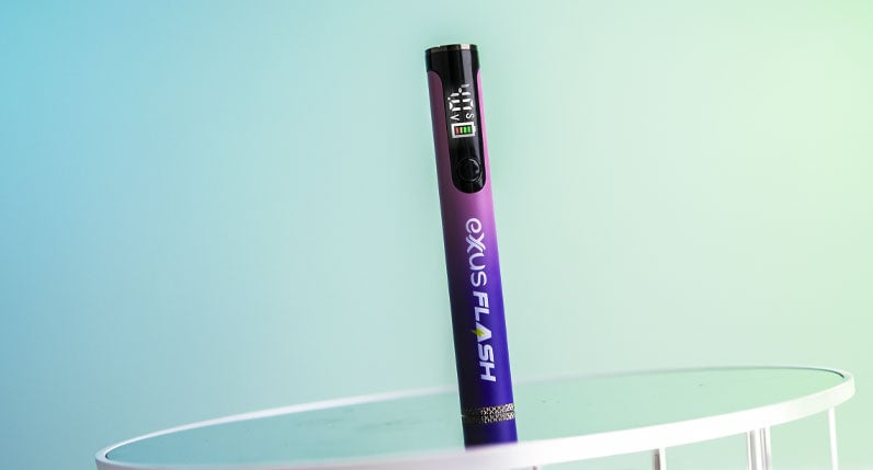 Exxus Flash cartridge vaporizer standing on a table against a pale blue background