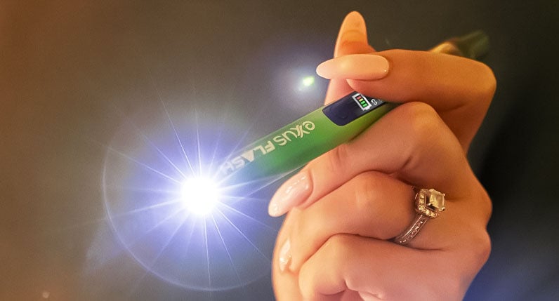Hand holding a green Exxus Flash cartridge vaporizer with its flashlight lit