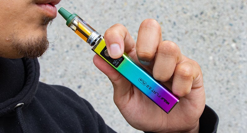 Person holding a rainbow WULF Flat Plus 2.0 510 thread battery with a cartridge attached