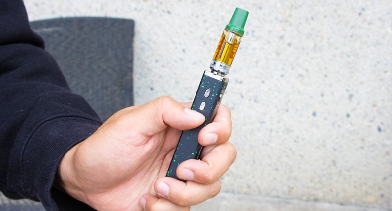 Hand holding a black WULF Flat Plus 2.0 510 thread battery with a cartridge attached