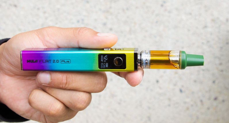 Hands holding a rainbow WULF Flat Plus 2.0 510 thread battery with a cartridge attached