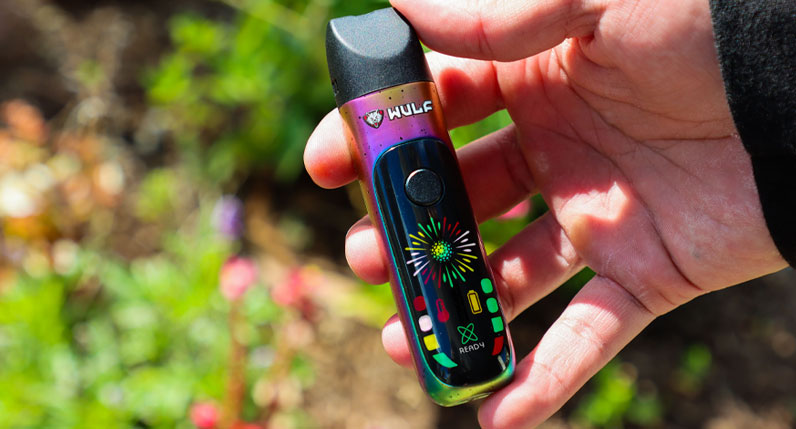 Hands holding a rainbow WULF Budr portable concentrate vaporizer outdoors
