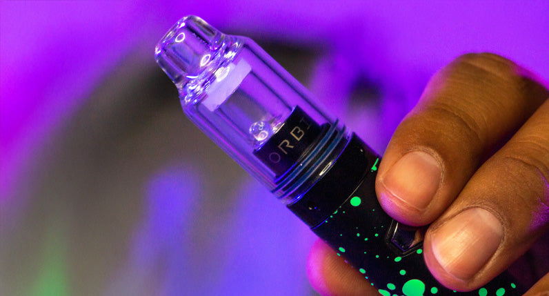 Hand holding a WULF Orbit concentrate vaporizer under purple lighting